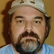 Dark-haired man with a round face and dark facial hair, wearing a baseball cap